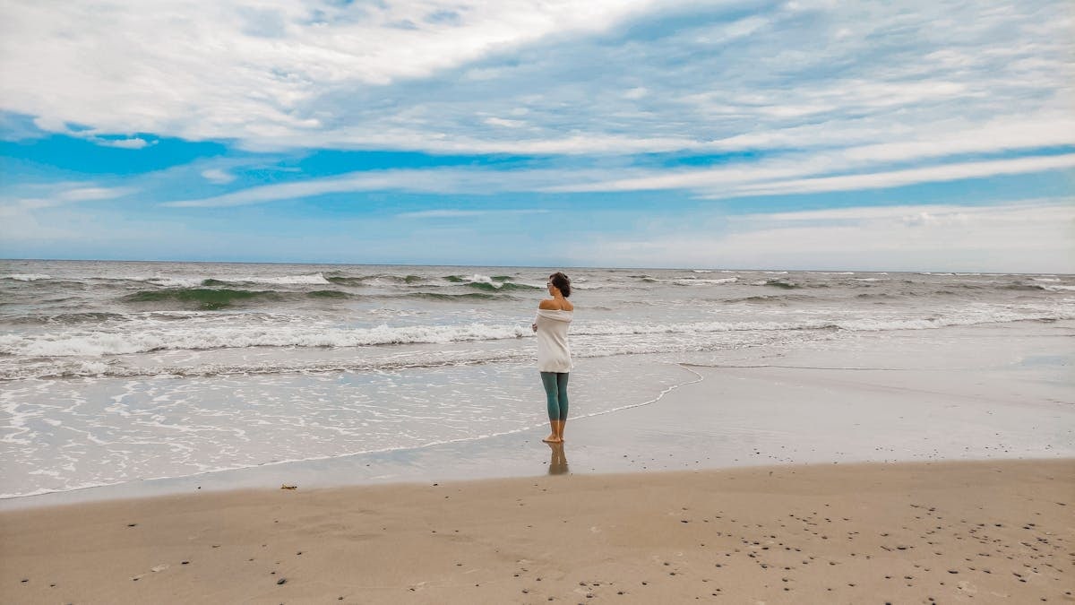 A woman stands peacefully by the Baltic Sea in Łeba, Poland during the daytime.